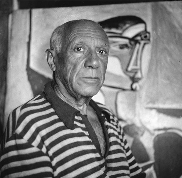 Pablo Picasso, black-and-white portrait in a striped shirt in front of a painting